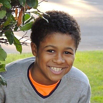 A young boy smiling for the camera in front of a tree.