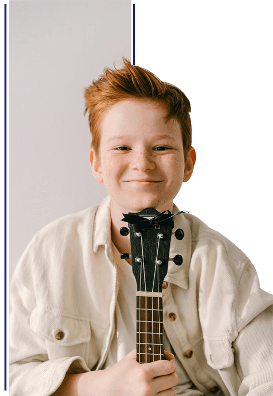 A young boy with red hair and a white shirt is holding his guitar.